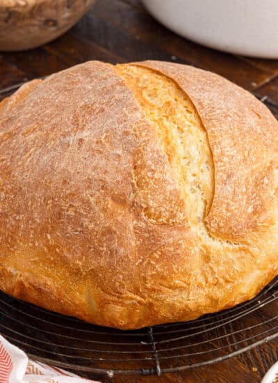 Loaf of Dutch Oven Bread on the wood cutting board, with ingredients in the background and text overlay.