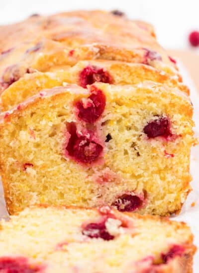 Slices of orange cranberry bread tilted against the loaf set on parchment paper and a cutting board.